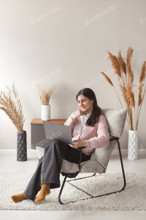 Preview: Attractive confident woman working remote on laptop from home with trendy interior