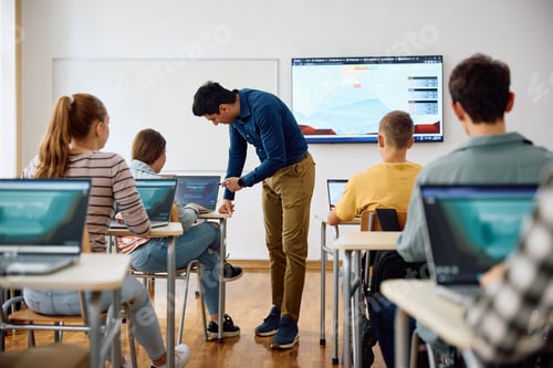 Preview: Computer science teacher assisting his students in coding on laptop during a class at high school.