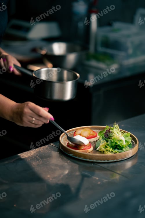 Preview: in a professional kitchen on clean metal table a woman chef collects a salad with fresh meat and