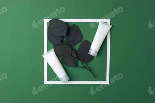 Preview: White tubes of cosmetic cream with white frame and eucalyptus on green background