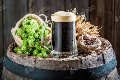 Preview: Dark beer with foam, wheat and hops on old barrel