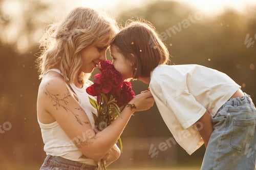 Preview: Mother with her little daughter is on the field with red flowers