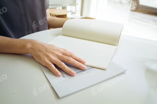 Preview: Close up and selective focus hands opening and holding blank book or magazine on table.