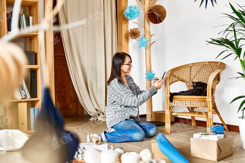 Preview: Woman using cell phone and play with black cat while wrapping christmas gifts in craft recycled pape
