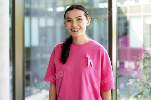 Preview: Young woman smiling and wearing pink ribbon for breast cancer awareness