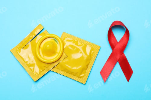Preview: Yellow condoms and red ribbon on light blue background, flat lay. LGBT concept