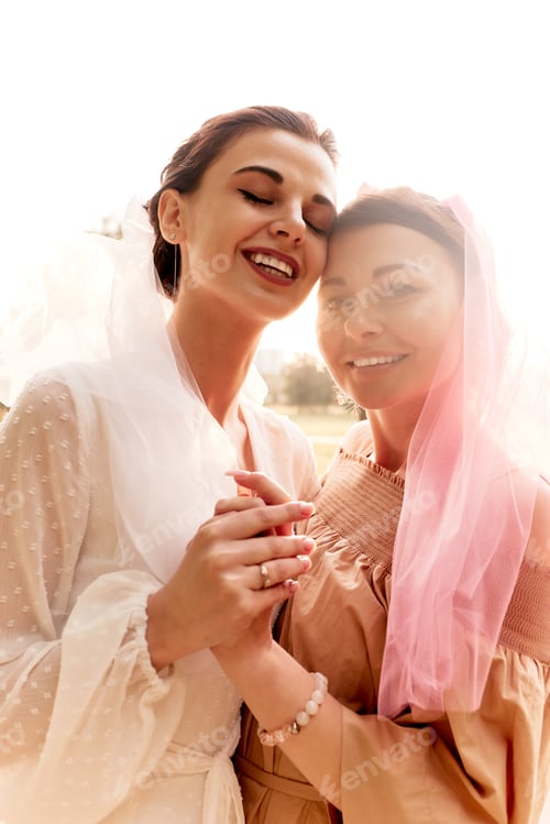 Preview: Happy charming bride in a white dress with white veil and a bridesmaid in a beige dress with pink