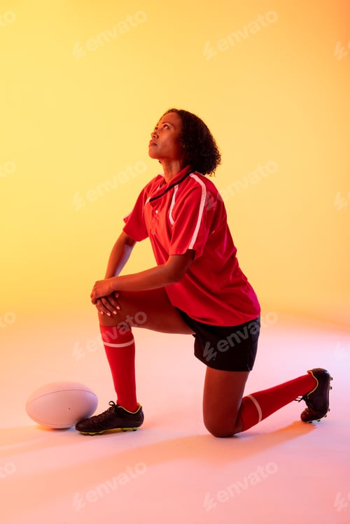Preview: African american female rugby player with rugby ball over neon yellow lighting