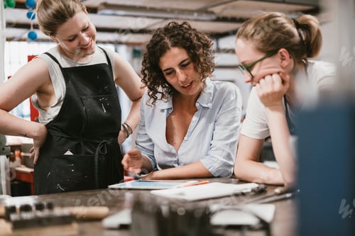 Preview: Three female jewellers looking at digital tablet at workbench meeting