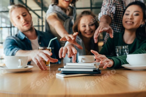 Preview: Young friends taking back their smartphones lying in pile on table in cafe