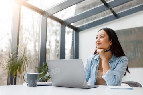 Preview: Thoughtful asian woman with laptop in sunny workspace