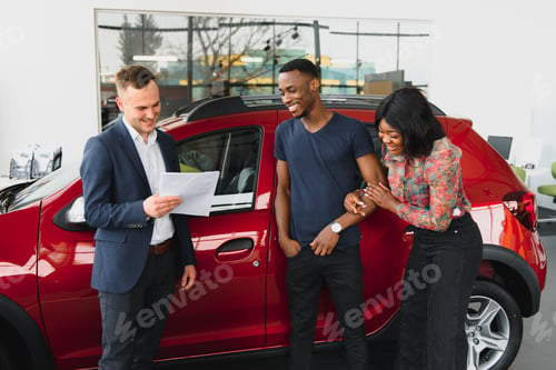 Preview: African american family at car dealership. Salesman is showing trunk of new red car.