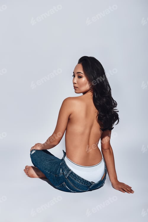 Preview: Pure beauty. Rear view of young woman looking over shoulder while sitting against grey background