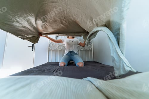 Preview: Young woman in bed arrange the sheet by throwing it in the air