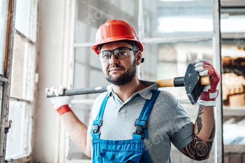 Preview: Muscular construction worker stands by the window and holds a big sledgehammer