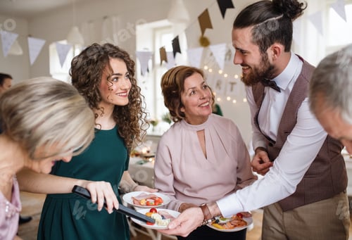 Preview: Multigeneration family putting food on plates on a indoor family birthday party.