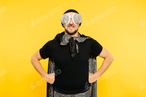 Preview: Man Dressed as Superhero Fly Insect With Goggles and Cape Against Vibrant Yellow Background