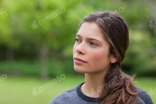 Preview: Thoughtful young woman standing in a park while looking towards the side