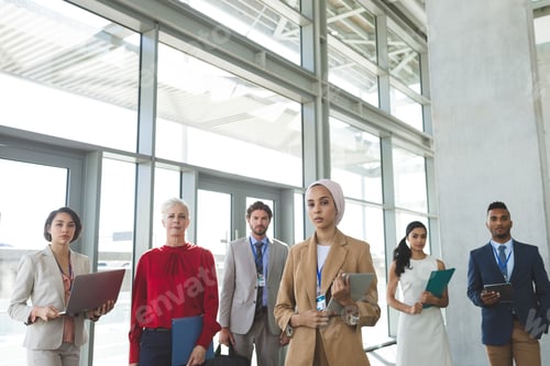 Preview: Portrait of mixed race business people looking at camera while standing in modern office building