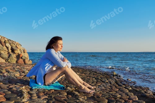 Preview: Mature woman sitting on the seashore enjoying the seascape, nature, sunset