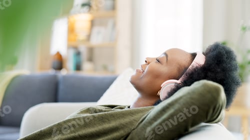 Preview: Young woman listening to music while relaxing on a sofa at home. Carefree, cheerful and happy femal