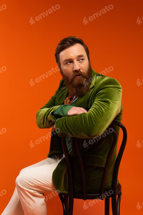 Preview: Portrait of stylish bearded man sitting on chair on red background