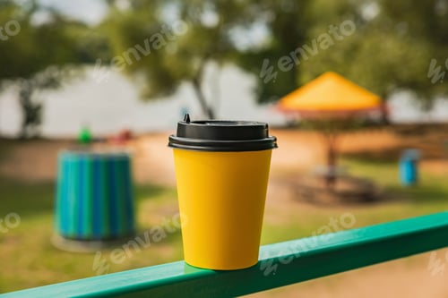 Preview: Bright yellow takeaway coffee cup outside, recreation area in bokeh