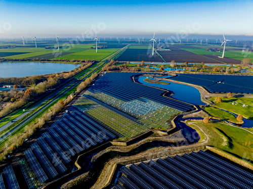Preview: Aerial view of a sprawling solar farm amidst green fields with wind turbines in the background