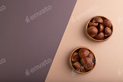 Preview: wooden bowl with raw edible Сhestnuts on brown and gray paper pastel, top view, flat lay, copy space