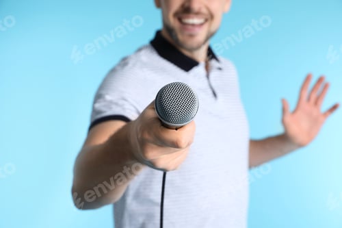 Preview: Handsome man in casual clothes holding microphone on color background, closeup