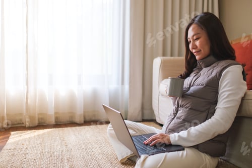 Preview: Portrait image of a young woman drinking coffee while working on laptop computer at home