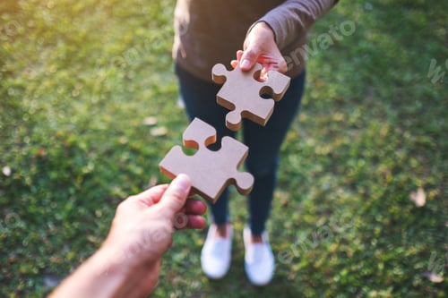 Preview: Closeup image of two people holding and putting a piece of wooden jigsaw puzzle together