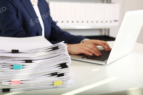 Preview: Stack of documents and woman working with laptop at table in office, closeup