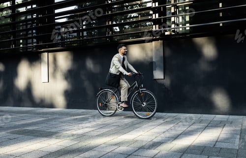 Preview: Businessman riding bicycle in front of modern office building.