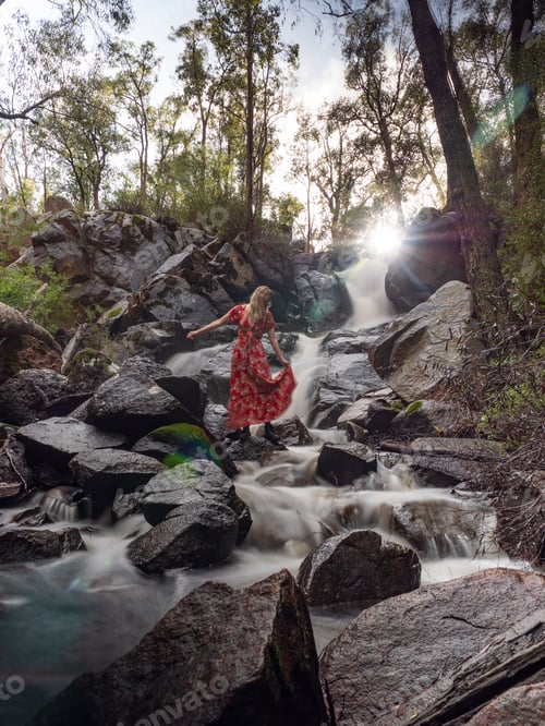 Preview: Beautiful shot of a woman posing at the rocky waterfall
