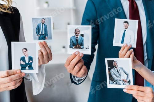 Preview: cropped view of recruiters touching photos while standing in office