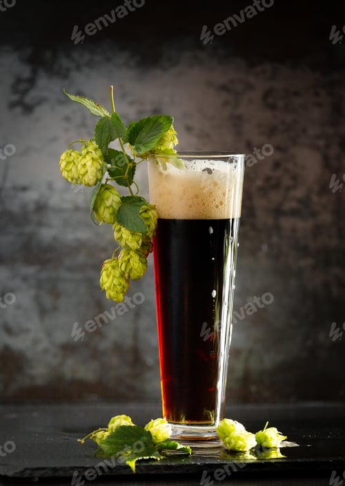 Preview: Glass of dark beer with hops around on a dark background