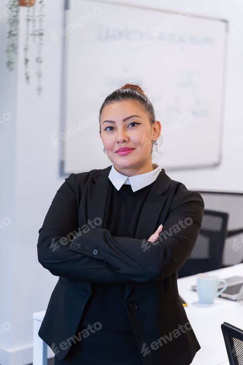 Preview: Businesswoman posing with her arms crossed while standing in the office.