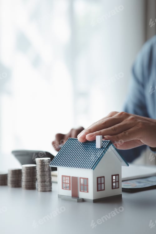 Preview: People with house models and piles of coins are calculating.