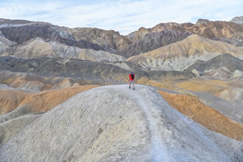 Preview: Colorful minimalism hiker on top a hill in Death Valley desert badlands of the 20 mile mile canyon