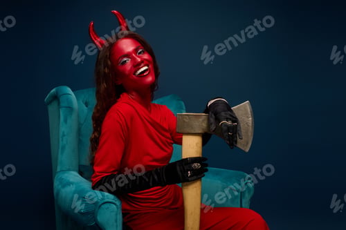 Preview: A captivating woman in a devil costume joyfully poses with an axe in a vibrant blue setting
