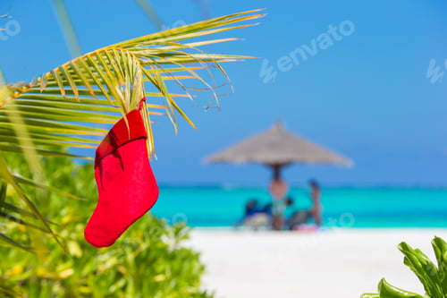 Preview: Red Santa Christmas stocking between palm trees on white beach