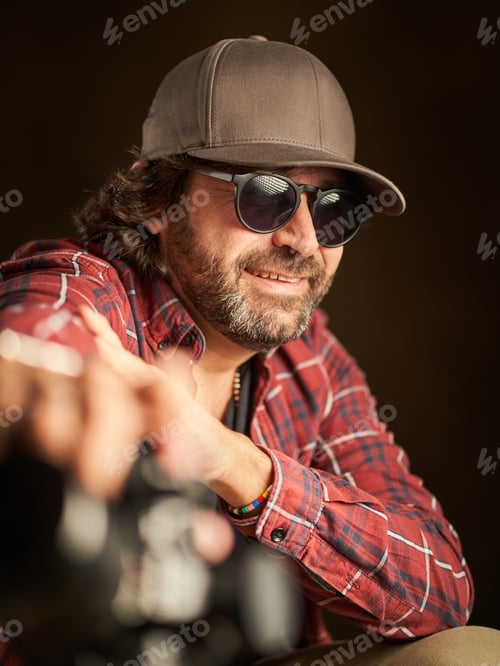 Preview: Portrait of a quiet man smiling with an amused gesture wearing a cap and sunglasses