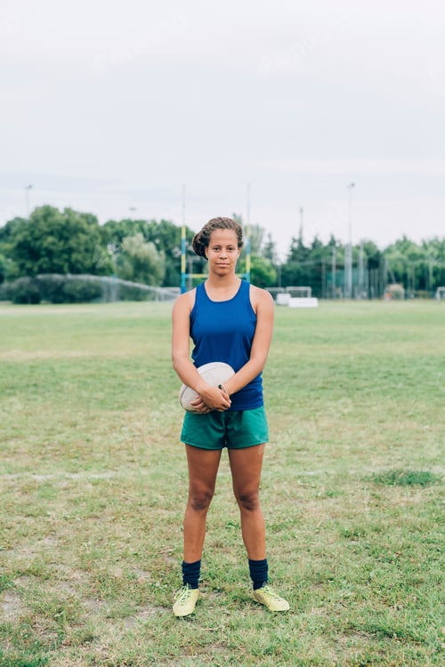 Preview: Confident athlete holding a rugby ball on the field