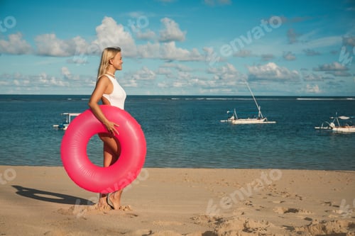 Preview: Woman stands on sandy beach holding a float ring