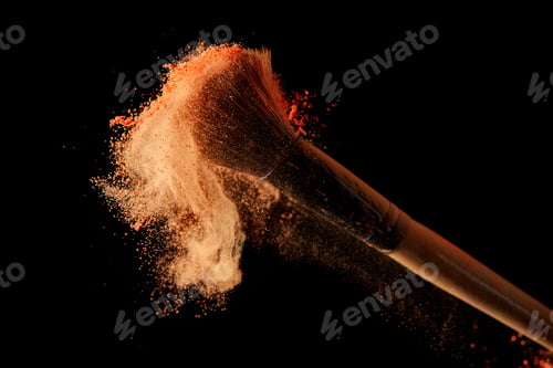 Preview: cosmetic brush with orange powder explosion on black background
