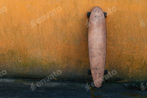 Preview: Worn skate longboard leaning against the dirty orange wall