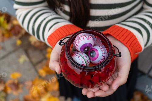 Preview: Child holding jar of halloween eyeballs amidst colorful autumn leaves