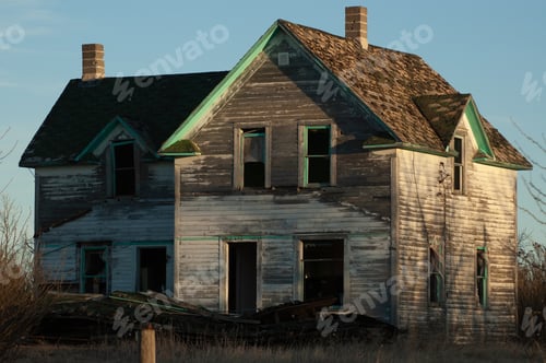 Preview: Creepy, old and aged abandoned wooden house in a field under the blue sky