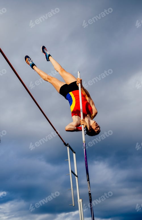 Preview: Female pole vaulter in mid-air over the bar against a cloudy sky backdrop